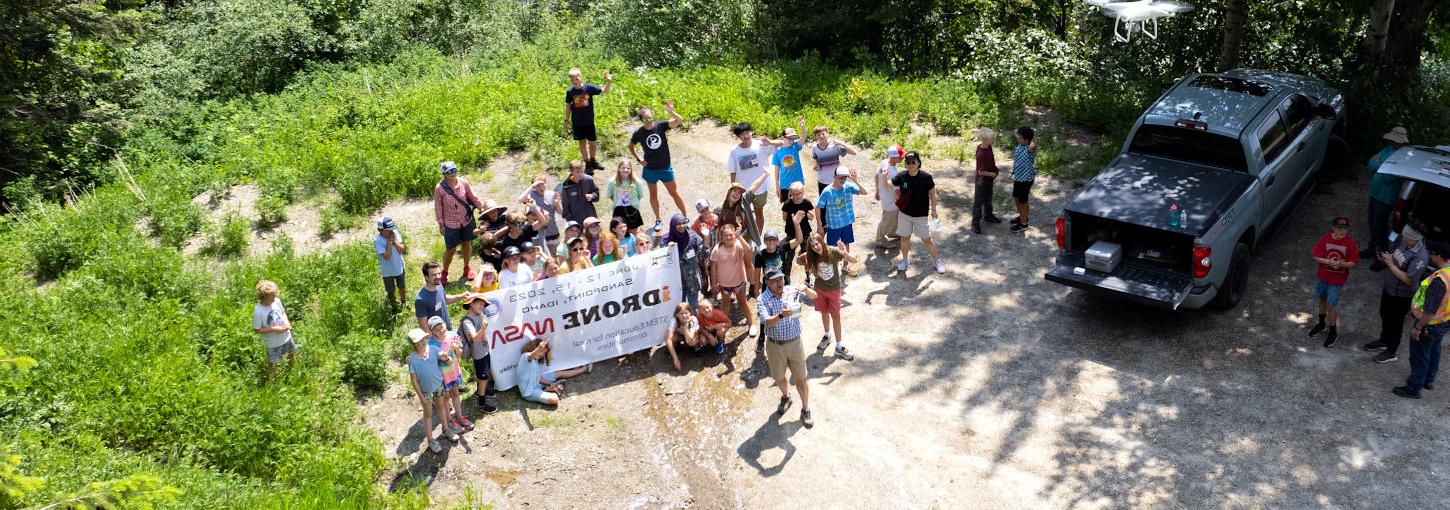 Drone photo of group standing on the ground holding a banner.